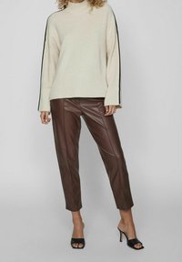 Crème ribbeltrui met zwarte zijkanten, gecombineerd met bruine faux leren broeken en zwarte open-teen haksandalen.