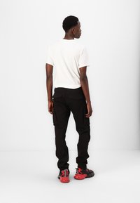 Vit t-shirt med kort ärm, svarta cargobyxor med fickor och svarta/röda sneakers. Minimalistisk design med fokus på funktionalitet.