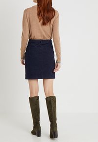 Chemise marron à manches longues, jupe en velours côtelé bleu marine, et bottes en daim vert olive jusqu'aux genoux avec talons bloc. Ajustement slim avec poches arrière.