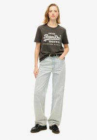Mørkegrå bomulds t-shirt med hvid grafisk tekst; lyseblå løstsiddende jeans; sorte snørebånd sko; rund halsudskæring; afslappet stil.