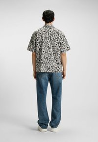 Camicia a maniche corte con un motivo di testo astratto in bianco e nero. Abbinata a jeans blu larghi e sneakers bianche.
