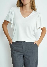 Top bianco a maniche corte con scollo a V e maniche a volant, abbinato a pantaloni grigi su misura. Tessuto morbido, design casual.