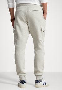 Ljusgrå sweatpants med en tapered design, sidofickor av cargotyp och ribbade muddar. I kombination med vita sneakers med mörka accenter.