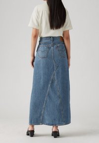 Blå denim långkjol med en figurnära midja, synliga bakfickor och sömdetalj som går ner i mitten. Bärs med svarta klackskor.