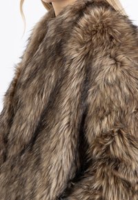 Abrigo de piel sintética en tonos marrones con una textura suave y mullida, que presenta un cuello alto y un ajuste suelto. Detalles vaporosos añaden dimensión.