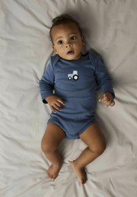 Blaues Baby-Bodysuit mit langen Ärmeln und Traktor-Print, aus weichem Stoff hergestellt, mit Druckknöpfen am Boden und bequemer Passform.