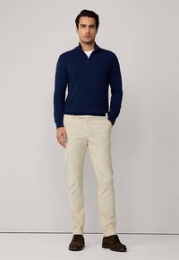 Navy ribbed quarter-zip sweater, cream chinos, and dark brown shoes. Smooth fabric texture, tailored fit, and simple design with no patterns.