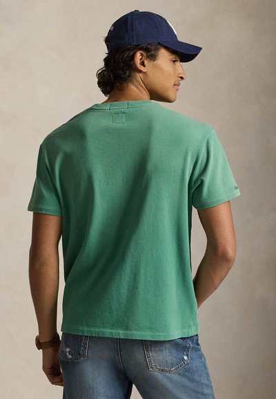 Πράσινο βαμβακερό t-shirt με κοντά μανίκια, ριμπ υφή και στρογγυλή λαιμόκοψη, συνδυασμένο με ανοιχτόχρωμα τζιν και μπλε σκούφο.
