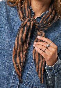 Braun und schwarz gestreifter Schal aus weichem Stoff, zu einem Knoten gebunden, getragen mit einer Jeansjacke. Verfügt über einen goldenen Hardware-Akzent.