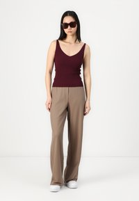 Top sin mangas de canalé burdeos con escote en V, combinado con pantalones de pierna ancha beige y zapatillas blancas. El modelo lleva grandes gafas de sol oscuras.