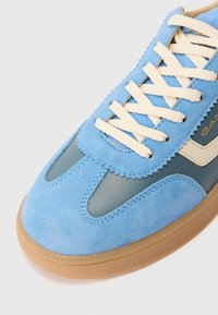 Sneaker in camoscio blu con sovrapposizione in pelle verde, lacci crema e suola in gomma color talco. Presenta una cucitura zigzag e il logo del marchio.