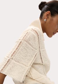 Pull en crochet de couleur crème clair, avec un motif carré, une texture en maille ouverte et des manches larges, doté d'un col replié.