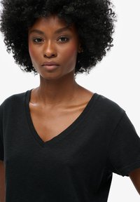 Zwarte V-hals T-shirt van zacht materiaal, met korte mouwen en subtiele branding aan de linkerkant van de borst.