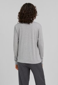 Graues Langarmshirt aus Baumwollmischgewebe, mit lockerer Passform und Rundhalsausschnitt, zeigt minimale Nähte und eine weiche Textur.