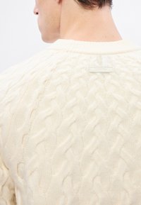 Krém színű kötött pulóver, texturált mintával, bordázott kerek nyakkivágással és hátul kis "Calvin Klein" feliratos címkével.