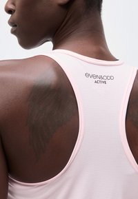 Gros plan sur le haut du dos et le cou d'une personne portant un débardeur Even&Odd Active rose pâle.