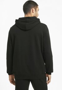 Sweat-shirt à capuche noir en tissu doux, présentant une coupe ample, des poignets côtelés et une poche kangourou, vu de l'arrière.
