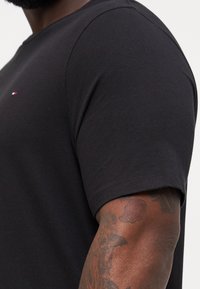 Svart bomull crew-neck t-skjorte med korte ermer og en liten brodert logo i rødt, hvitt og blått på brystet.
