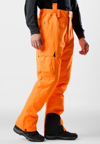 Felgekleurde oranje outdoorbroek met verstelbare banden, meerdere zakken en versterkte zwarte onderbenen. Gemaakt van duurzaam materiaal voor robuust gebruik.