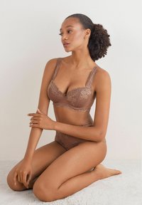 Brązowy komplet bielizny – koronkowy biustonosz i pasujące majtki, zdobiony kwiatowymi wzorami, z teksturowanej tkaniny, wyposażony w szerokie ramiączka i dekoracyjne wykończenia.
