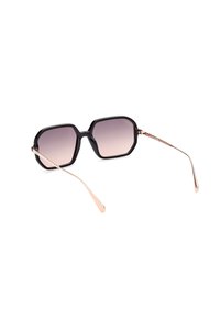 Occhiali da sole ottagonali con montatura in plastica nera e lenti sfumate. Tempistiche sottili in metallo rosa dorato. Superficie liscia, design moderno.