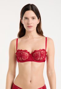 Soutien-gorge rouge avec bonnets en dentelle transparente ornés de broderies florales, bretelles réglables et bords festonnés. Bande lisse et armatures.