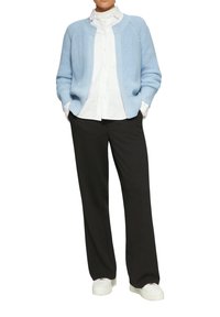 Hellblauer Strickcardigan über einem weißen Hemd mit Knöpfen, kombiniert mit schwarzen weit geschnittenen Hosen und weißen Sneakers.