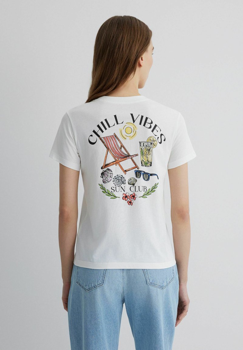 White cotton t-shirt featuring back graphic with "CHILL VIBES," sun, deck chair, drink, sunglasses, seashells, and floral accents.