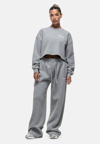 Felpa grigia a maniche lunghe con colletto a girocollo e testo ricamato, abbinata a pantaloni larghi coordinati con vita elasticizzata.