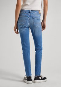 Smalle blauwe jeans van denim met een vervaagde textuur, voorzien van achterzakken met zigzagstiksels. Draag met zwarte sneakers.