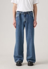 Wide-leg blue denim jeans with a faded wash, featuring a button and zipper fly, belt loops, and large front pockets.