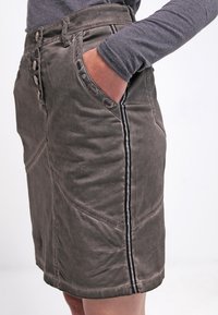 Grijze, knielange rok met een gestructureerde afwerking, voorzien van een knoopsluiting aan de voorkant, zijzakken en een zwartgestreepte accent langs de naad.