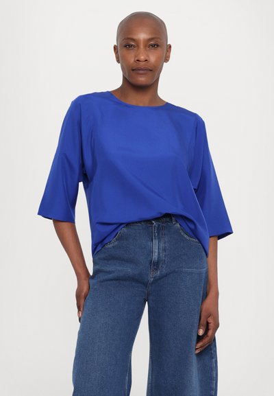 Sininen lyhythihainen toppi pyöreällä kaula-aukolla ja joustavalla kankaalla, yhdistettynä korkeavyötäröisiin, leveisiin denim-farkkuihin. Yksinkertainen muotoilu ja puhtaat linjat.