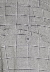 Tessuto grigio con motivo a scacchi bianco e nero, caratterizzato da una tasca con patta fissata da un singolo bottone grigio.