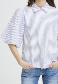 Overhemd met knopen in wit en lichtblauwe strepen. Korte pofsleeves, kraag en een losse pasvorm. De stof lijkt licht en gestructureerd.