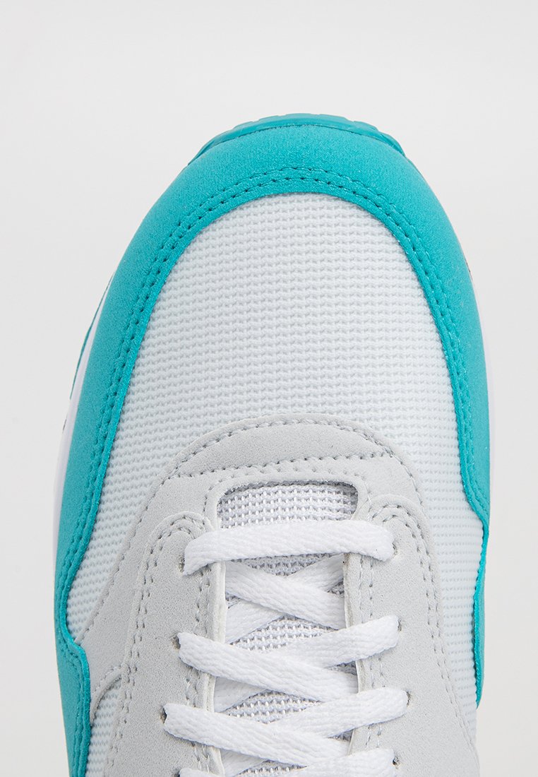 Lichtgrijze sneaker met een gestructureerde bovenkant van stof, turquoise accenten en witte veters. Heeft een gladde neus en mesh panelen.