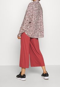 Camiseta fluida de manga larga con base blanca y patrón abstracto en rosa y negro; combinada con culottes anchos de canalé en rojo óxido y zapatillas negras.