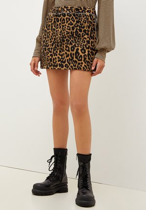 Mini gonna in stampa leopardata realizzata in tessuto morbido, con tasche frontali e indossata con stivali combat neri con lacci.