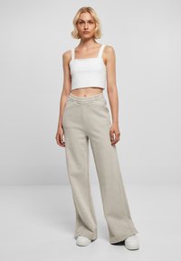 Witte cropped tanktop met vierkante halslijn, gecombineerd met lichtbeige wijdgevallen joggingbroek met een elastische tailleband en zijkanten.