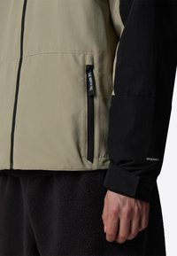 Letvægts tofarvet jakke med beige krop og sorte ærmer. Inkluderer en lynlåslomme og "WINDWALL" detalje på manchet.