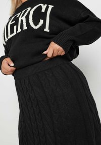 Mustat neulottu villapaita, jossa on "MERCI" vaalean cream-värisin kirjaimin, yhdistettynä mustaan vaipponeulehameeseen, jossa on ribbattua vyötäröä ja teksturoitua kuviota.