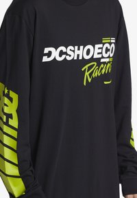 Μαύρο μπλουζάκι με μακρύ μανίκι από βαμβάκι. Διαθέτει λευκά και νεον πράσινα λογότυπα και σχέδια στα μανίκια. Σχέδιο κλασικού λαιμού τύπου crew.