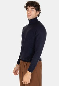 Maglione a collo alto blu navy realizzato in un materiale liscio, con un design aderente e maniche lunghe. Etichetta del marchio discreta in basso.