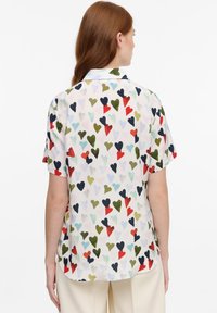 Blusa a maniche corti in tessuto leggero con un motivo di cuori multicolori su sfondo bianco. Colletto classico e design con orlo curvo.