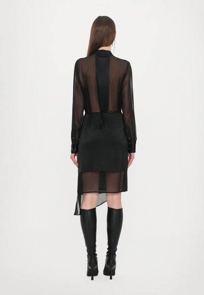 Black sheer dress with long sleeves, a tie at the waist, and a high-low hem; worn with knee-high black boots.