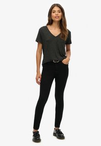 Zwarte v-hals t-shirt gemaakt van een gestructureerde stof, gecombineerd met slim-fit zwarte jeans. Schoeisel bestaat uit zwarte veterschoenen met een strikaccent.