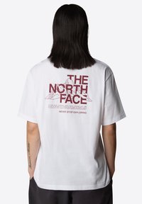 Camiseta de algodón blanca con un gráfico rojo en la parte posterior que presenta el texto "THE NORTH FACE" y un diseño de montaña, de mangas cortas y ajuste relajado.