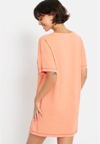 Peach-colored cotton t-shirt dress with short sleeves, a relaxed fit, and contrasting pink stitching along the hem and sleeves.