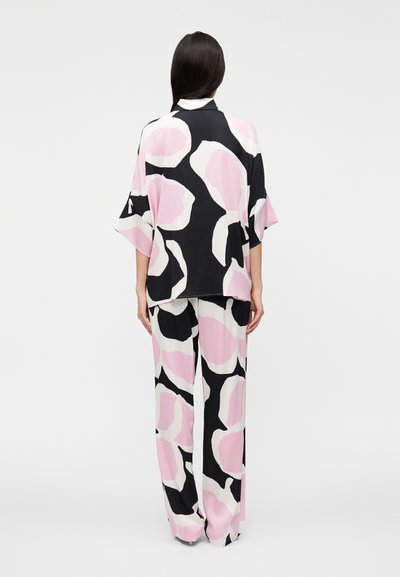 Σετ άνετης ενδυμασίας με σχέδια, που περιλαμβάνει ένα χαλαρό μαύρο μπλουζάκι με ροζ και λευκές αφηρημένες μορφές και παντελόνι φαρδύ με το ίδιο σχέδιο.