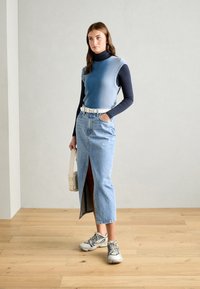 Ljusblå ribbad ärmlös topp över en marinblå rullkrage, parat med en högmidjad denimkjol med en framslits och vit bälte.